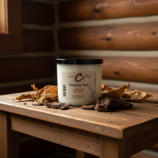 Tobacco Oud Soy Candle - 20 oz. 3 wick candle on a wooden table surrounded by dried leaves and bark.