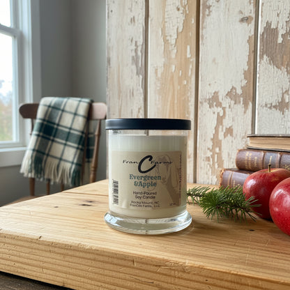 Evergreen and Apple Soy Candle - 12 oz. jar on wooden table with apples and greenery, creating a cozy home atmosphere.