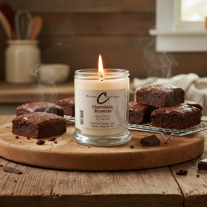 Chocolate Brownie Soy Candle lit next to freshly baked brownies on a wooden table.
