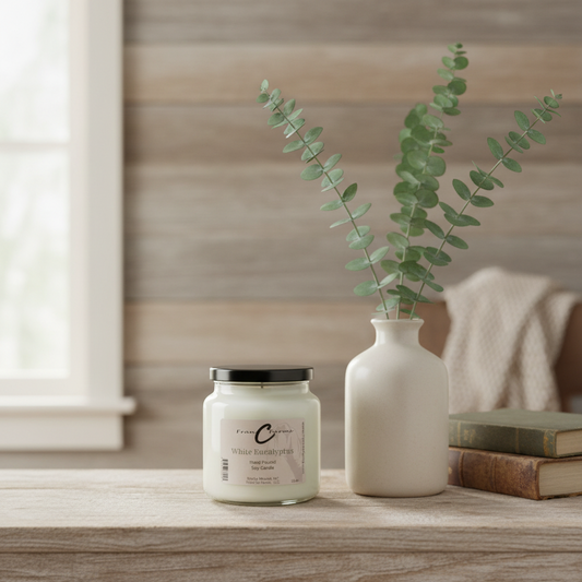 White Eucalyptus Soy Candle in an apothecary jar on a wooden table with a vase and eucalyptus branches.