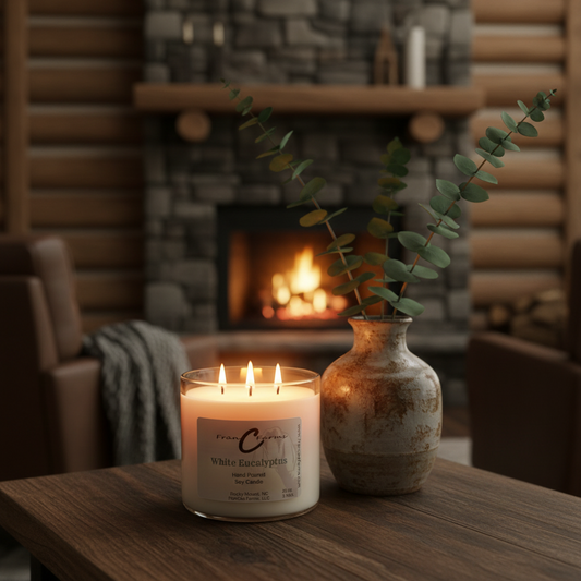 White Eucalyptus Soy Candle - 20 oz. 3 wick burning on a table next to a decorative vase and a cozy fireplace.