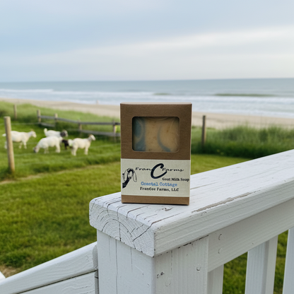 Coastal Cottage Goat Milk Soap packaging displayed on a railing with a beach and goats in the background.