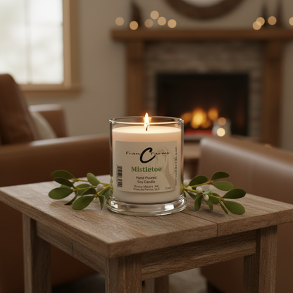 Mistletoe Soy Candle on a wooden table with green foliage, creating a cozy holiday ambiance by a fireplace.