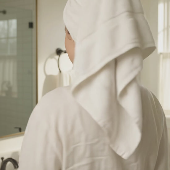 Woman in a white bathrobe holding an Ocean Breeze goat milk body wash pump bottle in a bathroom.