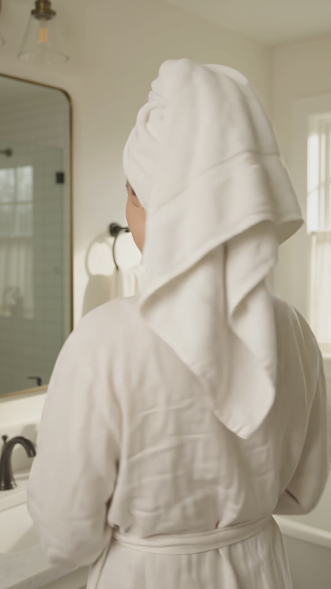 Woman in a white bathrobe holding an Ocean Breeze goat milk body wash pump bottle in a bathroom.