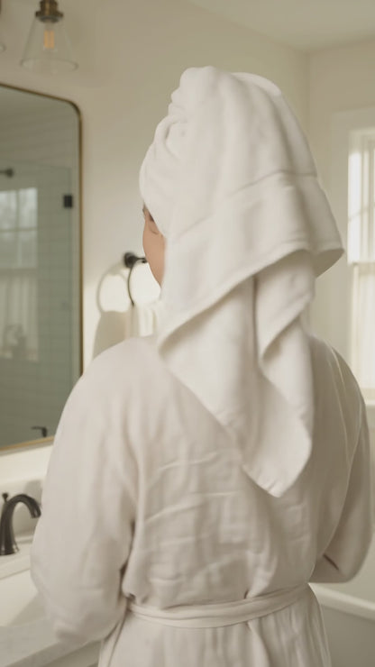 Woman in a white bathrobe holding an Ocean Breeze goat milk body wash pump bottle in a bathroom.